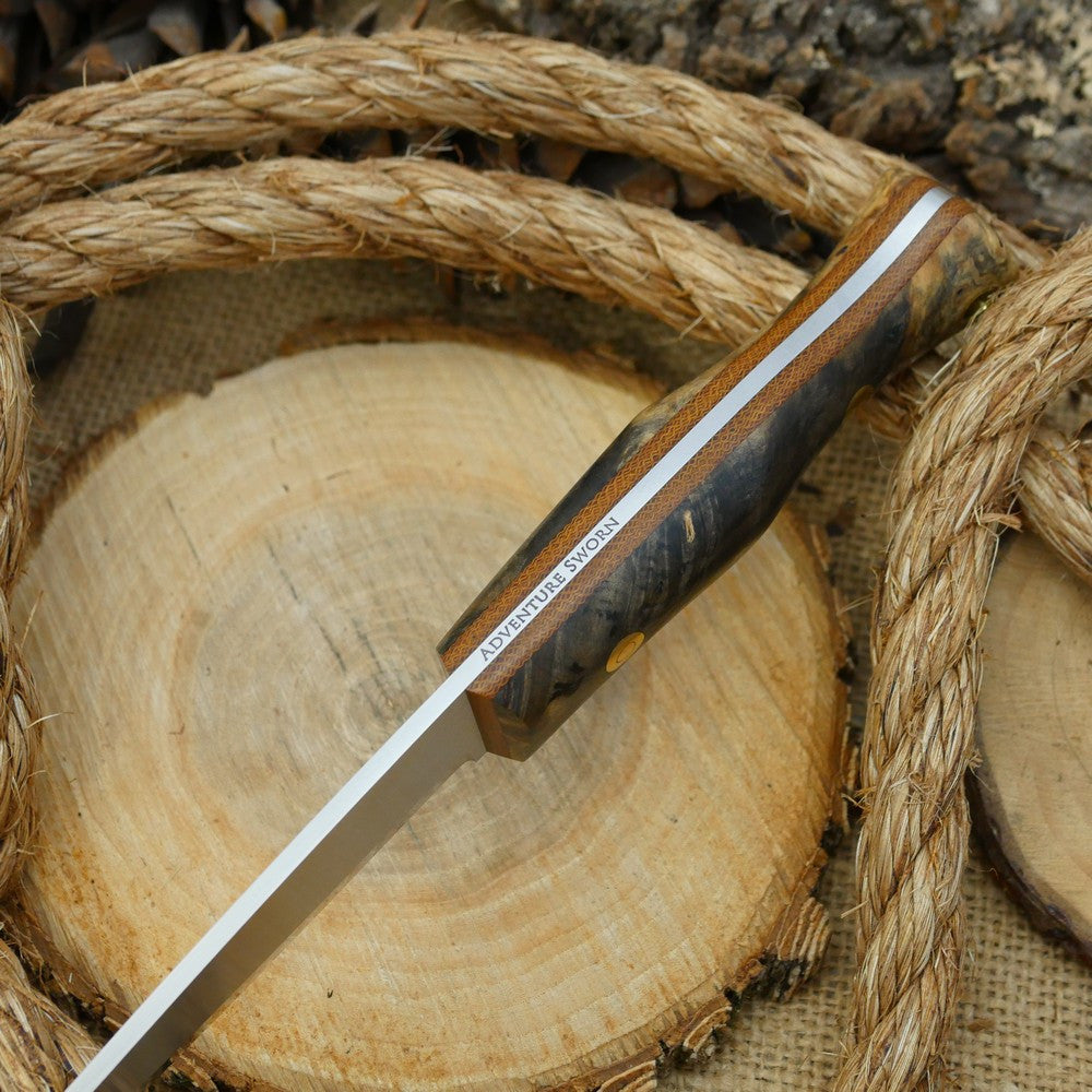 An Adventure Sworn Mountaineer bushcraft knife with Ohio buckeye burl handle scales and brown canvas liners.