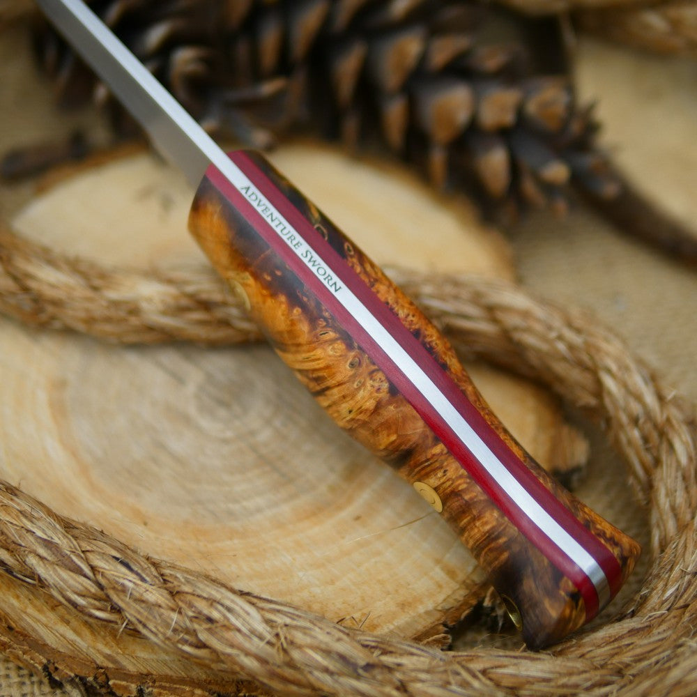 An Adventure Sworn Woodcrafter Bushcraft Knife with dyed box elder handle scales and 1/8 thick red liners