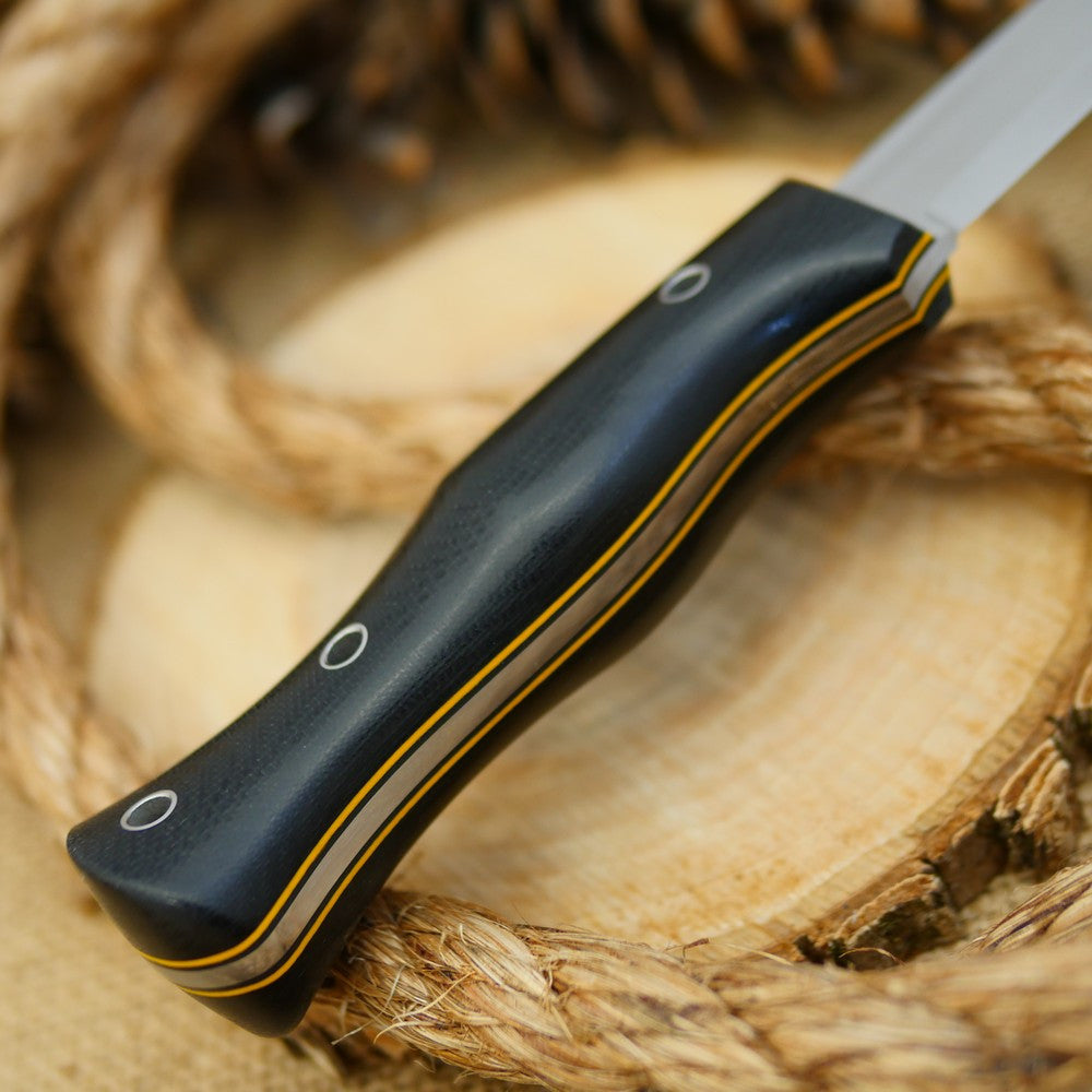 An Adventure Sworn bushcraft knife with black canvas micarta handle scales and black and yellow liners.
